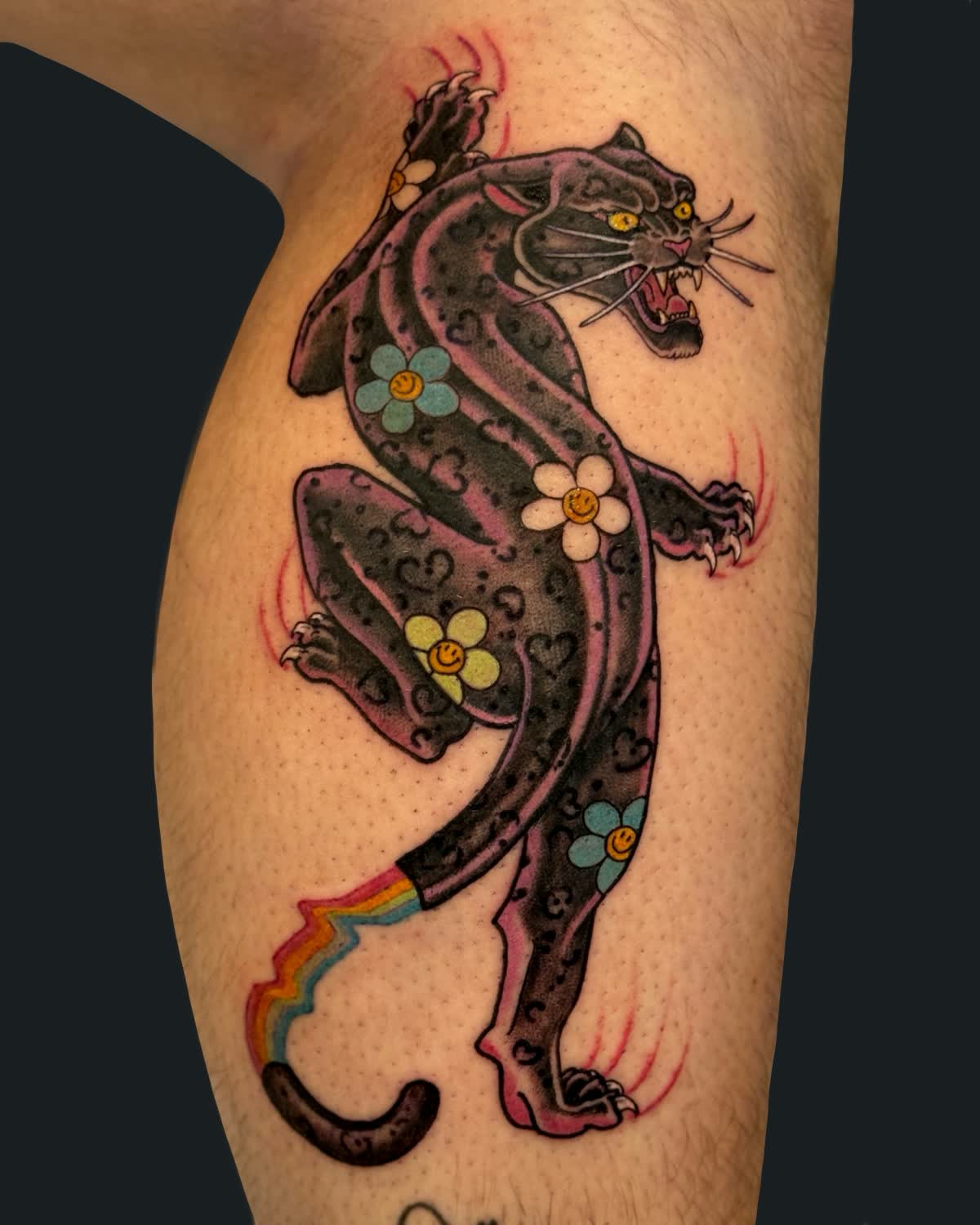 Psychedelic neo-traditional panther with smiling daisies and a rainbow tail, tattooed on a calf by English Cousins